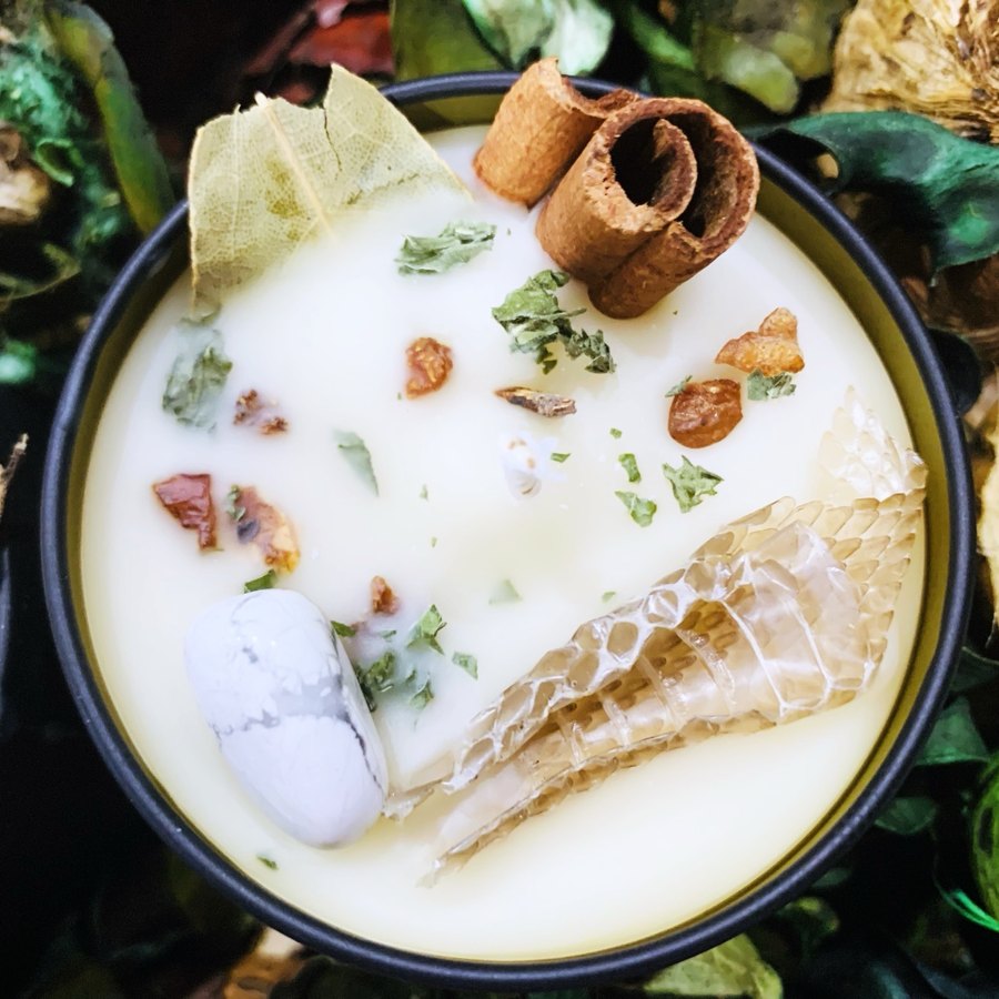 White intention candle topped with cinnamon, a bay leaf, botanicals, a white stone and a shed snakeskin
